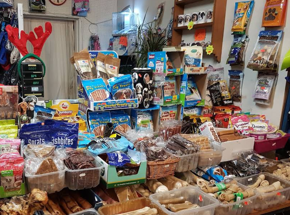 A retail display filled with assorted pet treats, bags of chews, and packaged snacks arranged on shelves and tables inside a store.